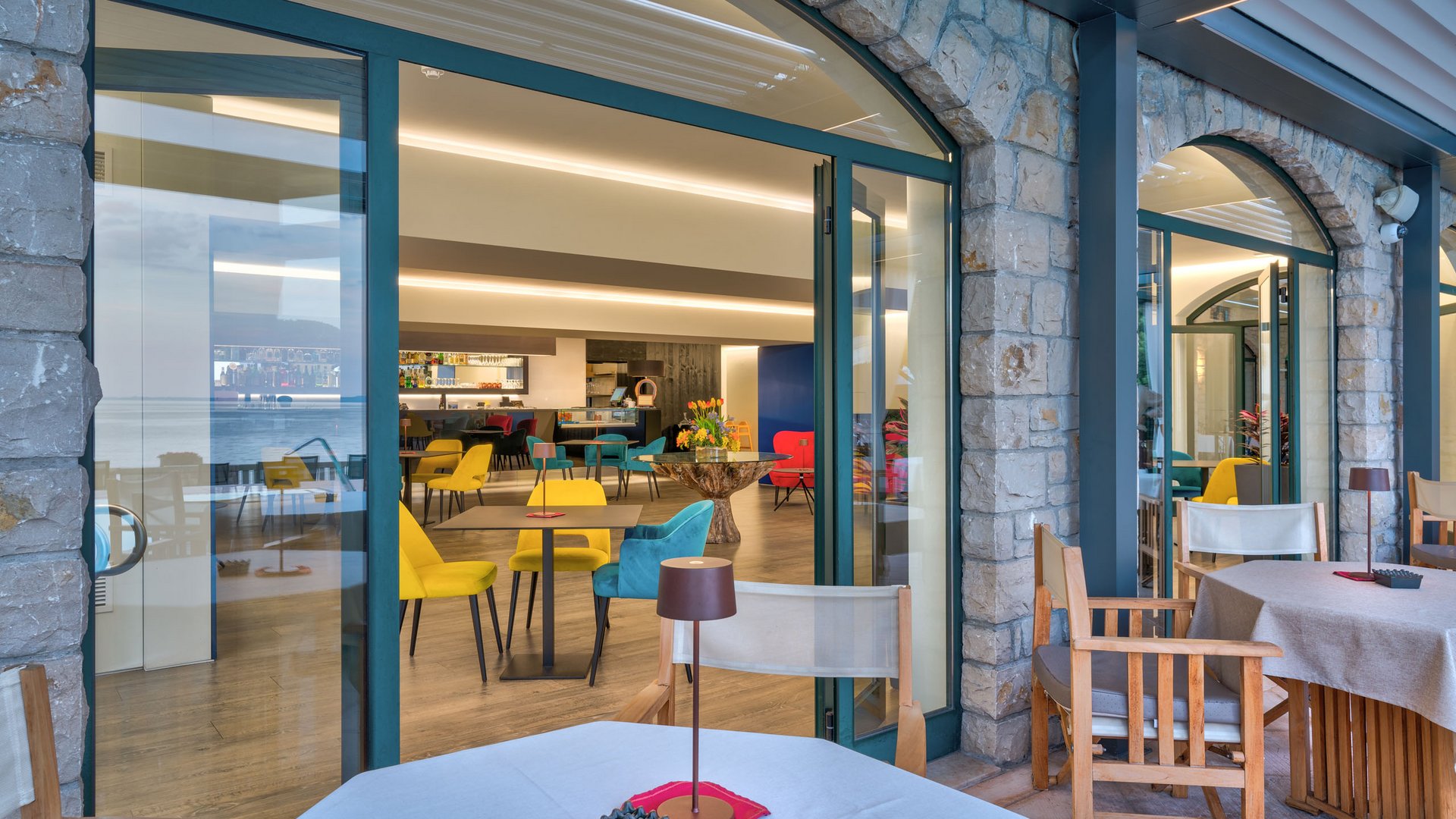A laid-back holiday on Lake Garda at a 4-star hotel Modern bistro area with colorful chairs and stone doors with glass
