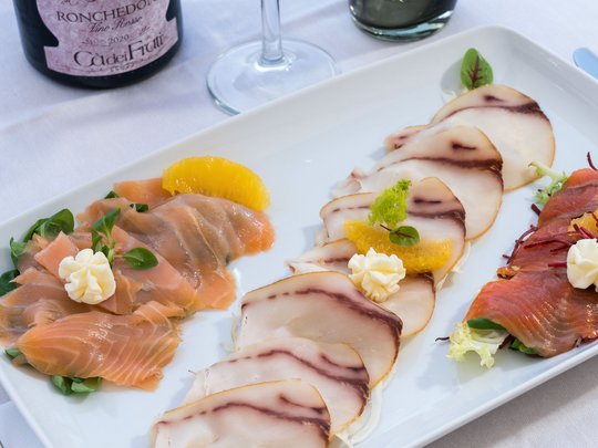 A laid-back holiday on Lake Garda at a 4-star hotel Three types of thinly sliced smoked fish with garnish on a white plate