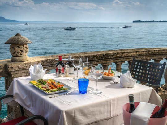 A laid-back holiday on Lake Garda at a 4-star hotel Set table with sea view and seafood dishes on a terrace