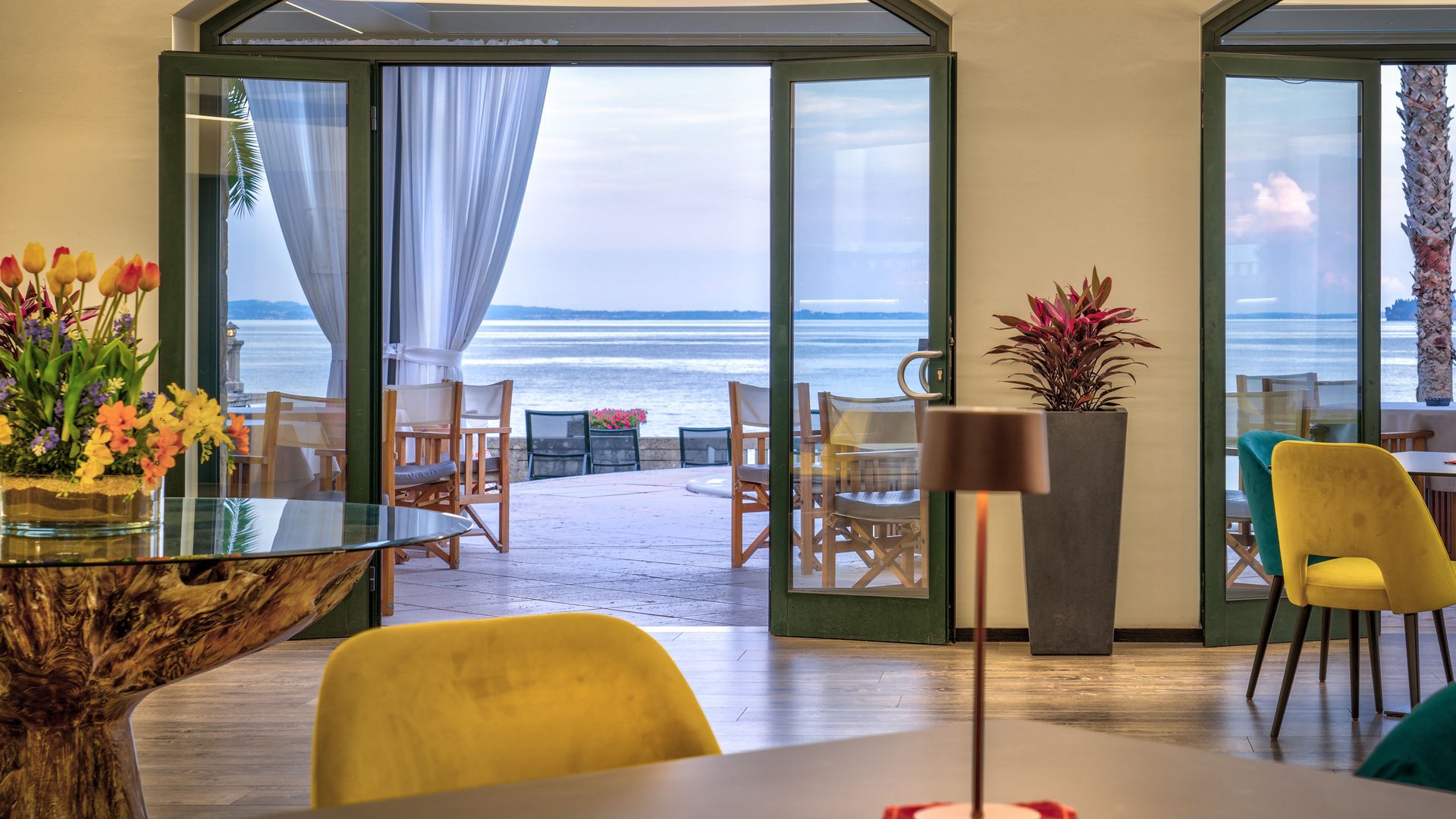 A laid-back holiday on Lake Garda at a 4-star hotel View through open room with chairs and table to terrace and lake