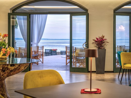 A laid-back holiday on Lake Garda at a 4-star hotel View through open room with chairs and table to terrace and lake