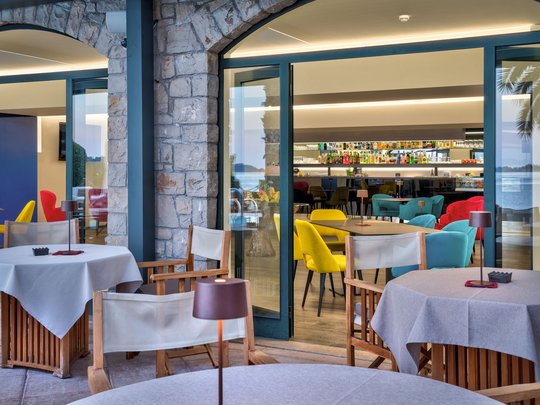 A laid-back holiday on Lake Garda at a 4-star hotel View of tables and colorful chairs in a modern café with a bar