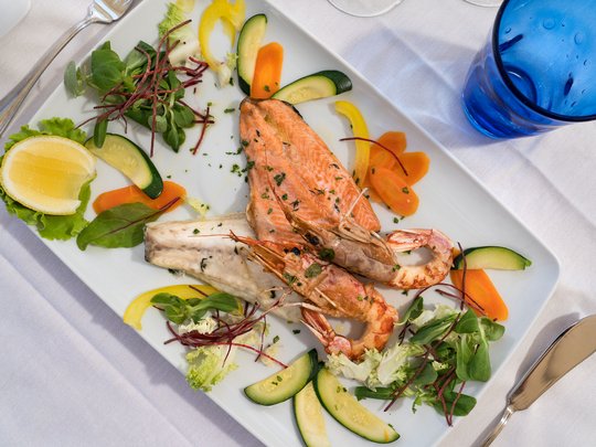 A laid-back holiday on Lake Garda at a 4-star hotel Plate with cooked fish, prawns, and sliced vegetables