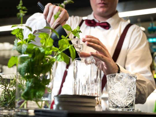 A laid-back holiday on Lake Garda at a 4-star hotel Bartender pouring ice into mixer with fresh herbs in foreground