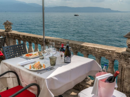 A laid-back holiday on Lake Garda at a 4-star hotel Table with wine and food on terrace overlooking lake and mountains