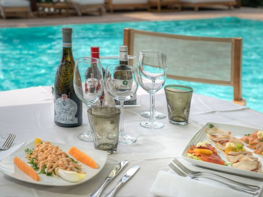 A laid-back holiday on Lake Garda at a 4-star hotel Table with wine, glasses, and appetizers next to a pool